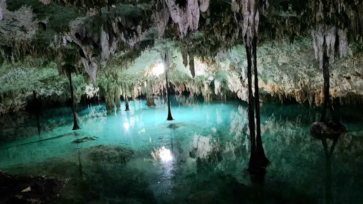 A guided swimmer under stalactites inside the Sac Actun cave system on a private cenote tour from Tulum